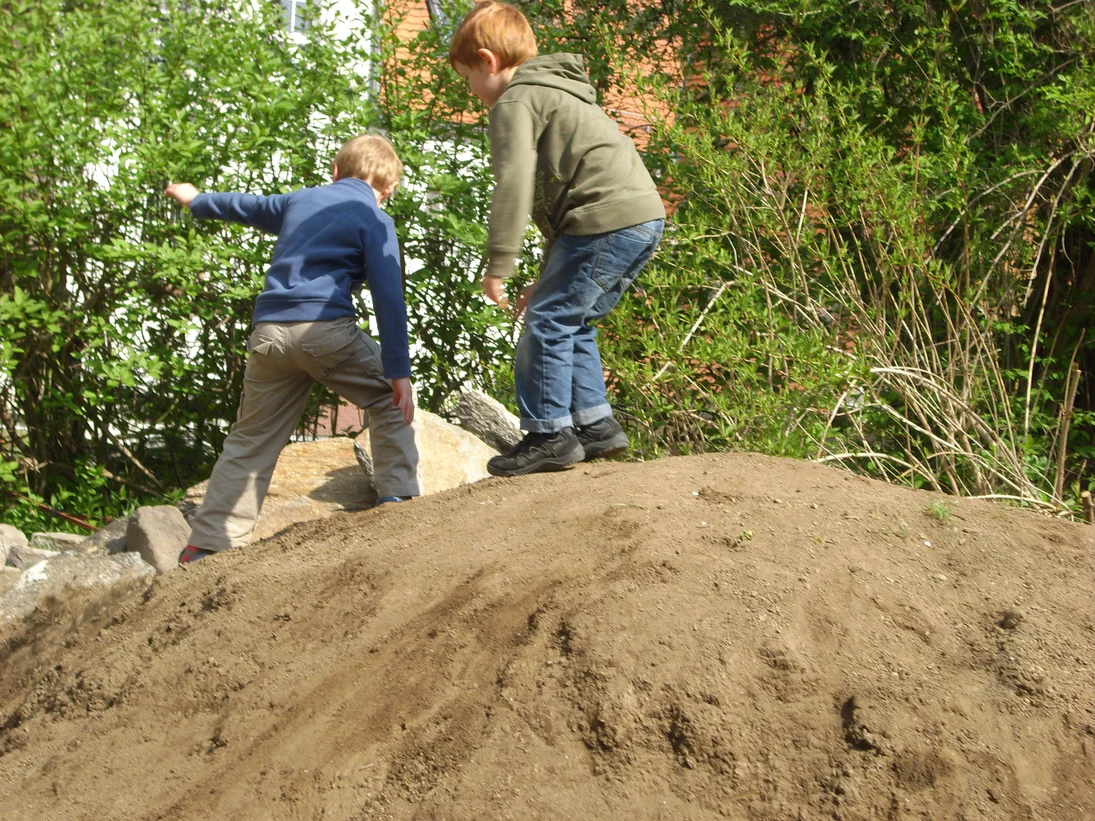 Das Bild zeigt spielende Kinder auf einem Sandhaufen.