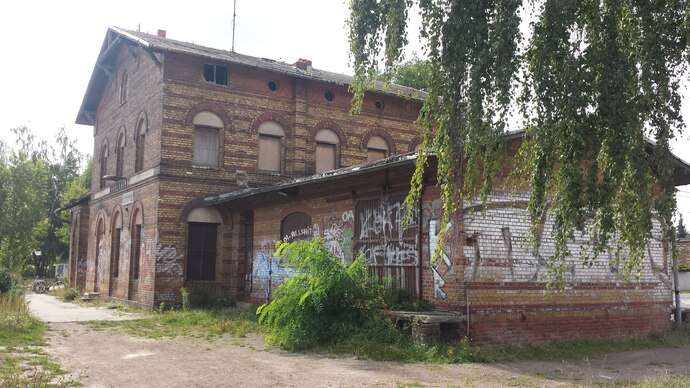 Das Foto zeigt eine Brachfläche im Grünen Ring Leipzig. Es ist ein ehemaliges Bahngebäude, aus Ziegeln bestehend, nun leerstehend und in ruinösem Zustand. Die Brachfläche wird als Infrastrukturbrache definiert.